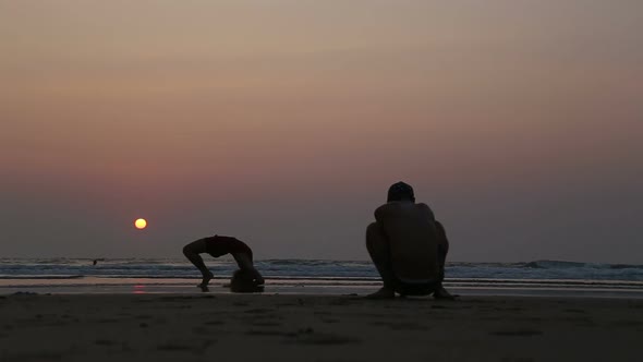 Man taking photos of woman stretching at beach in Goa at sunset.