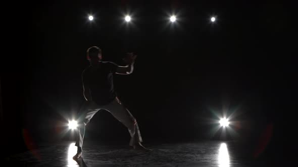 Man Practicing Capoeira in Darkness Against Spotlight in Studio