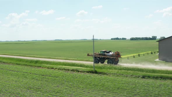 Tractor mounted pesticide sprayer driving on unpaved farm land dirt road. Aerial