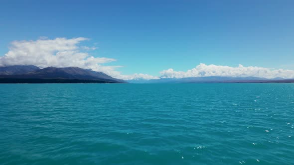 Low aerial view of colorful blue lake Pukaki in New Zealand. Aerial dolly crossing a turquoise lake