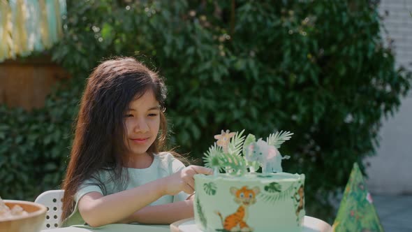 Little Girl Tries Cake and Looks at Camera at the Backyard Party on a Sunny Day