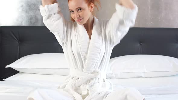 Redhead Girl in White Bathrobe on Bed in Hotel Room