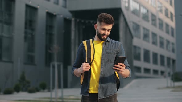 The Food Delivery Guy is Standing and Looking at the Smartphone