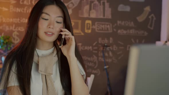 Attractive Asian Woman Talking on Mobile Phone Discussing Business Indoors in Dark Office