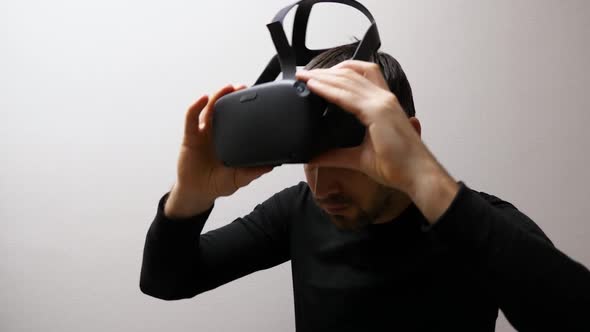 Close-up of a man at the gray wall putting VR glasses on his head and starting to dance