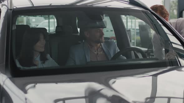 Couple Sitting in Car in Dealership and Listening to Salesman