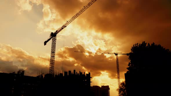 Silhouette of Tower Cranes Working on Construction Site Residential Golden Hour, Warm Cloudy Sky