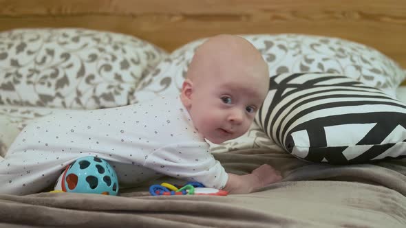 baby lies on the bed with toys and looks at the camera