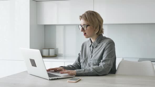 Blonde Lady Freelancer in Grey Shirt Types on White Laptop