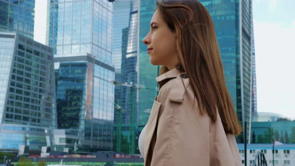 Brownhaired Woman Walks at Street in City Near Skyscrapers