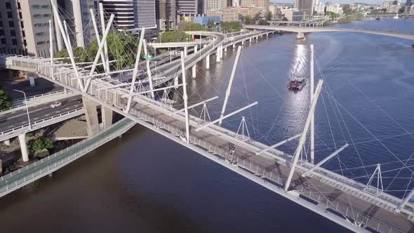 Aerial tilt shot of Kurilpa pedestrian bridge with City Cat sailing on river Brisbane, Queensland