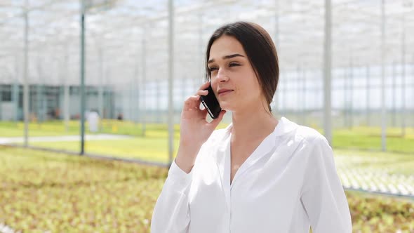 Worker Walking in a Greenhouse Using Mobile and Talking on Smartphone. Agricultural Engineer Working