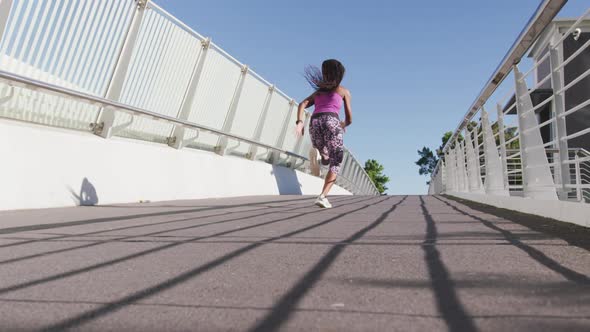 Rear view of african american woman running on the city bridge