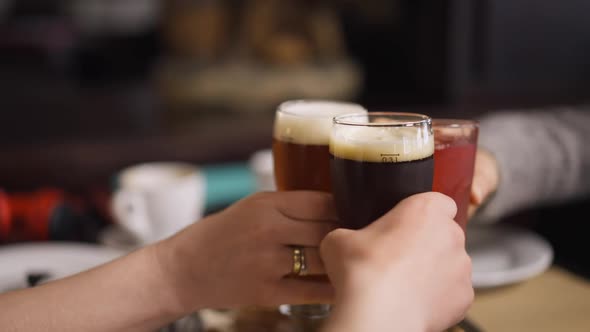 Closeup Hands Clinking Beer Glasses and Juice Over Table in Restaurant Indoors