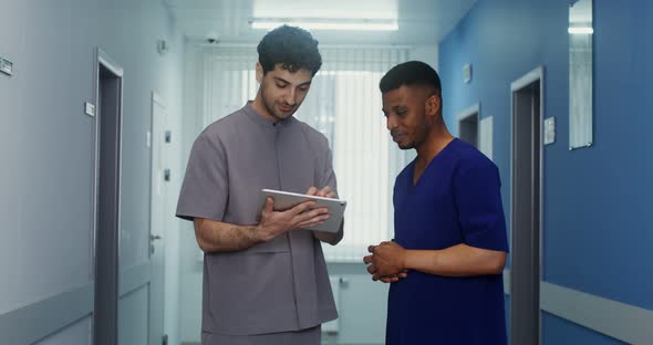 A Doctor Shows His Colleague Information on a Tablet in the Corridor of Clinic