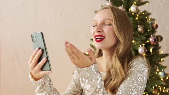 Festive woman making congratulation video call chat on mobile phone against of the christmas tree.