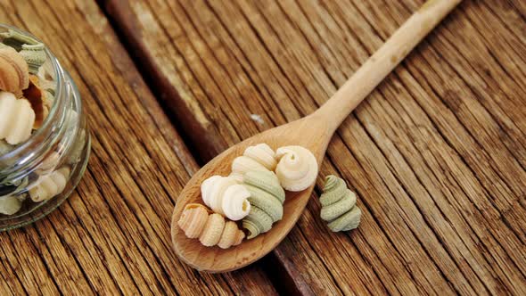 Colored half shell shaped pasta in jar and spoon on wooden background