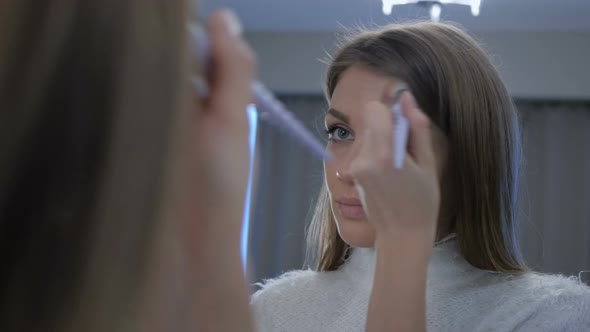 Young Woman Putting Make Up on Face in Mirror