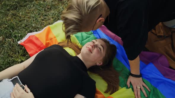 Genuine LGBT Couple Lying on Rainbow Flag and Smiling High Angle