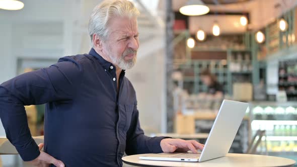 Old Man with Back Pain Using Laptop in Cafe