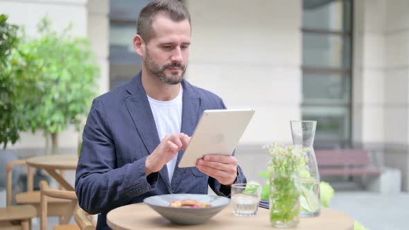 Man Browsing Internet on Tablet While Sitting in Outdoor Cafe