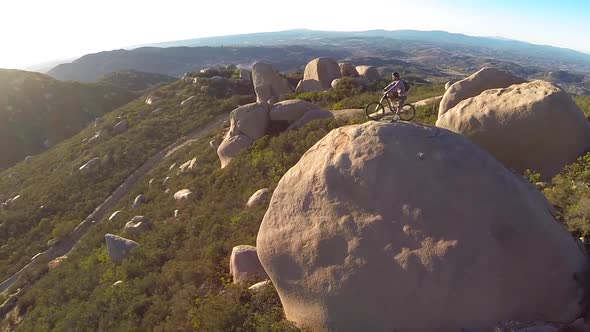 Aerial shot of young man mountain biker resting with his bike on a boulder.