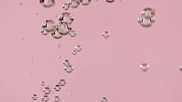 Macro Shot of Air Bubbles in Water Rising Up on Light Pink Background