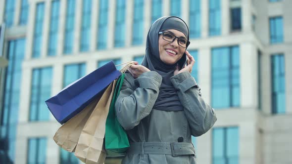 Happy Muslim Lady Chatting on Phone Outdoors Shopping Mall, Black Friday Sale