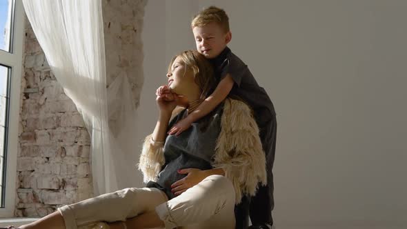 A Little Boy Gently Hugs Mom at Home Near the Window