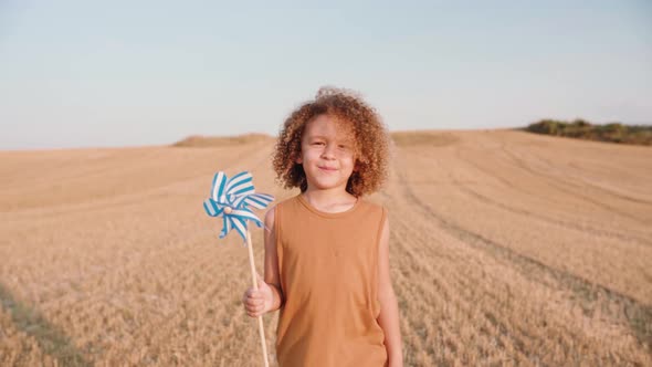 Portrait shot of smiling boy and windmill toy in hand walking over mowed field