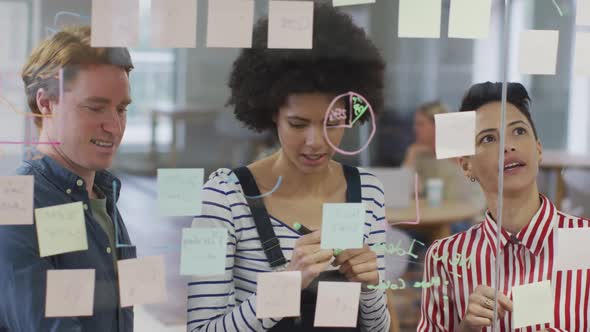 Diverse male and female business colleagues discussing by glass wall with memo notes