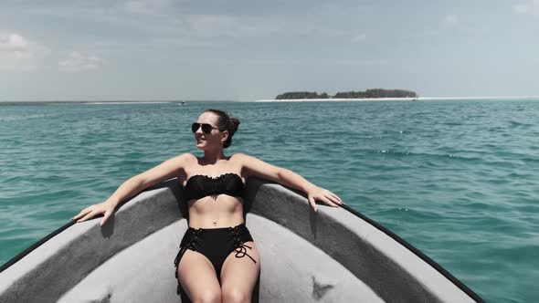 Young Woman in a Bikini and Sunglasses Lies on the Bow of Boat Floating By Ocean