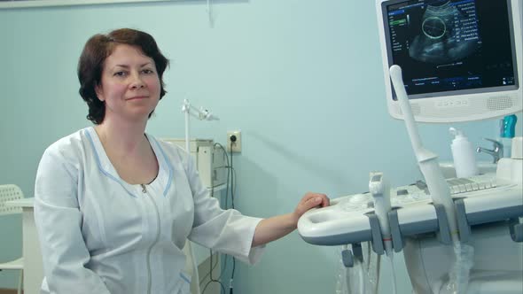 Smiling Female Doctor Sitting Next To Ultrasound Diagnostic Device