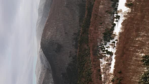 Aerial push in towards forest and foothill dusted in fresh snow. Vertical video