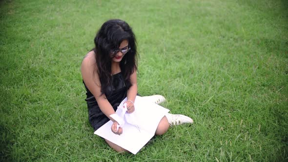 A depressed hot Asian girl is tearing the pages of a notebook with anger and throwing it on the grou