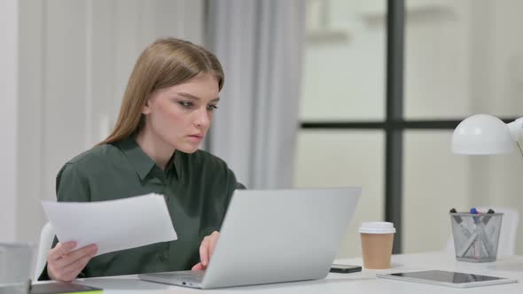 Young Woman Reading Documents While Working on Laptop