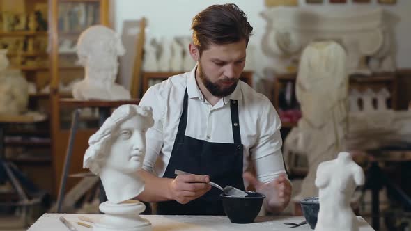 Young Male Master with Beard Preparing Mixture in Special Vassel for His Handmade Sculpture