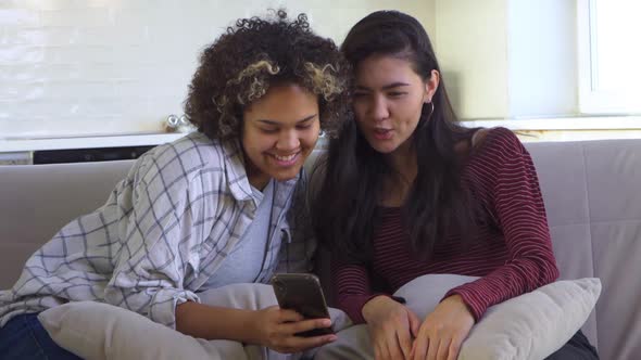 Two Girlfriends Looking at a Smartphone While Sitting on the Couch