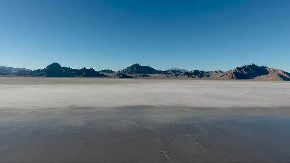 An aerial drone shot reveals smooth water covering the Bonneville Salt Flats and distant craggy moun