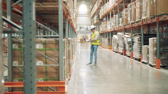 Storage Worker with a Laptop is Observing Shelves with Parcels