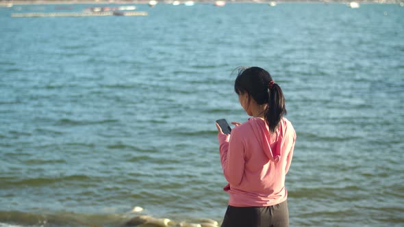 Asian sports female using a smartphone to checking social media while standing on the beach.