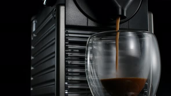 Black coffee machine pouring hot drink into the glass cup