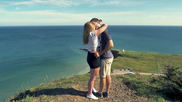 Man and woman kiss and embrace as they stand at a scenic overlook near a beautiful beach. Magdalen I