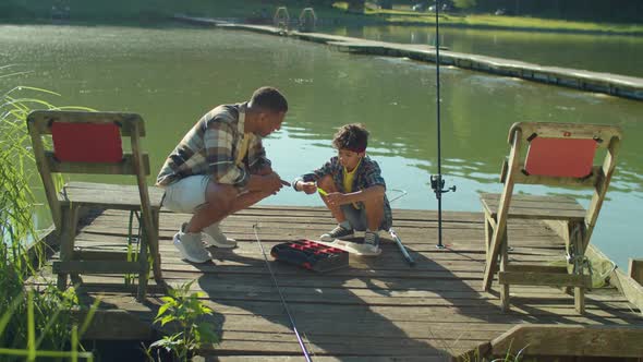 Skillful African Fisherman Telling to Teenage Boy About Fishing Lures By Lake