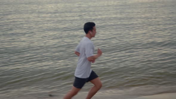 A handsome Asian sportsman running exercises outside on the beach in summer.