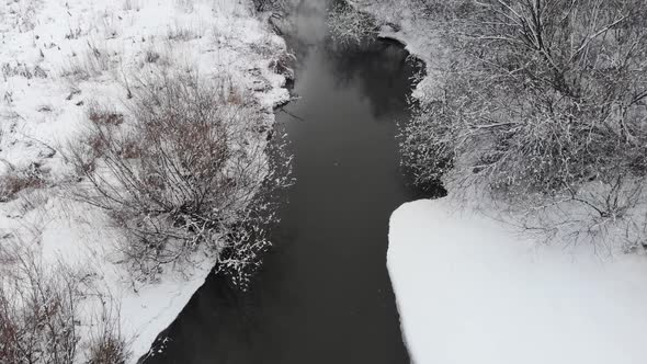 Top View - the Camera Moves Over the River. The Coast Is Covered with Snow. Aerial Video, Winter