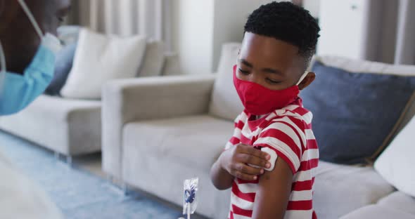 African american doctor wearing face mask gicing a lollipop to a boy after his vaccination at home