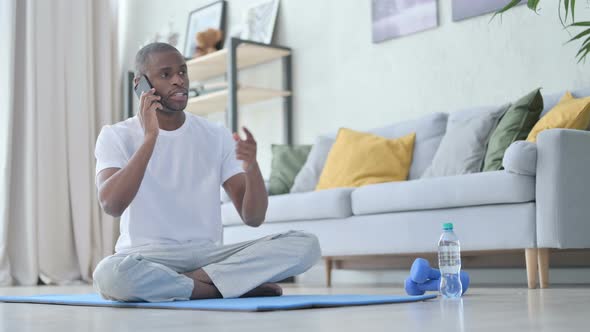 African Man Talking on Smartphone on Yoga Mat at Home