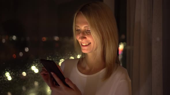 a woman uses a smartphone. The light from the phone illuminates the face.