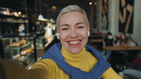 Woman Smiling and Waving During Video Call at Cozy Cafe